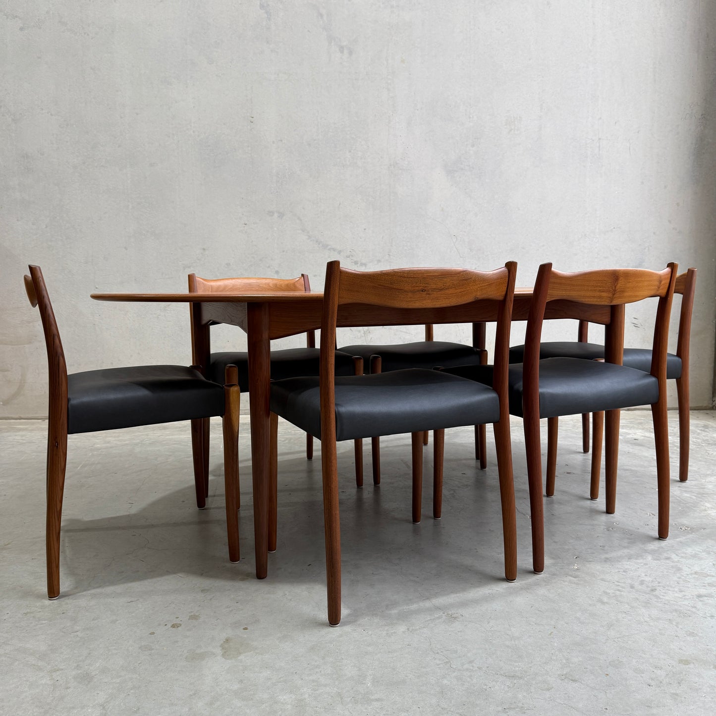 The Fully Restored Mid-Century Parker 91 Oval Teak Dining Suite with 6 Fler 64 Blackwood Chairs (Rediscover) offers timeless Australian elegance, perfect against a minimalist backdrop for sophisticated dining.