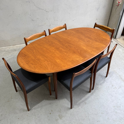 A fully restored Mid-Century Parker 91 oval teak dining suite with six Fler 64 blackwood chairs (Rediscover) is showcased on a light gray concrete floor against a plain, light-colored wall.