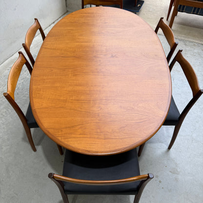 A fully restored mid-century Parker 91 oval teak dining suite with six Fler 64 blackwood chairs is arranged on a light concrete floor, showcasing its beautiful natural wood grain finish.