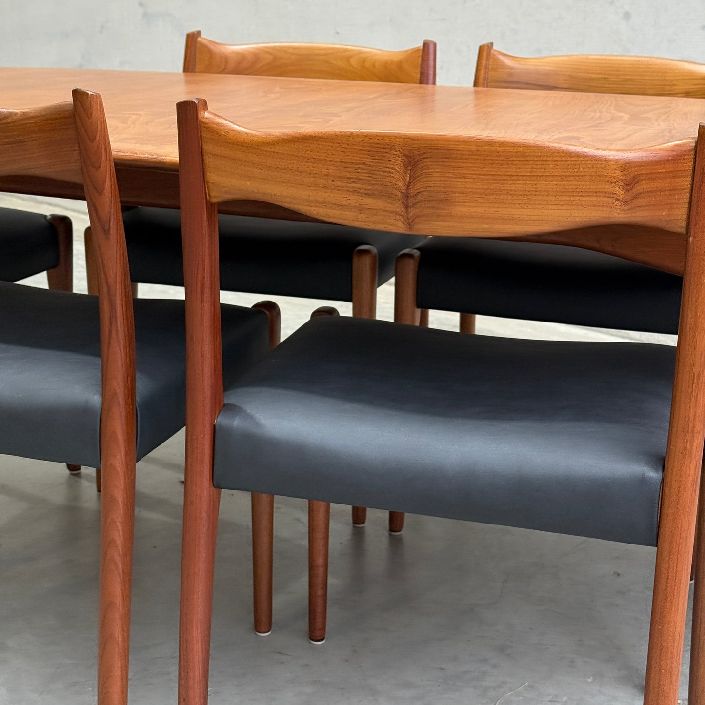 A close-up of a fully restored mid-century Parker 91 oval teak dining suite with six Fler 64 blackwood chairs, all from Rediscover, arranged on a light floor against a plain wall.