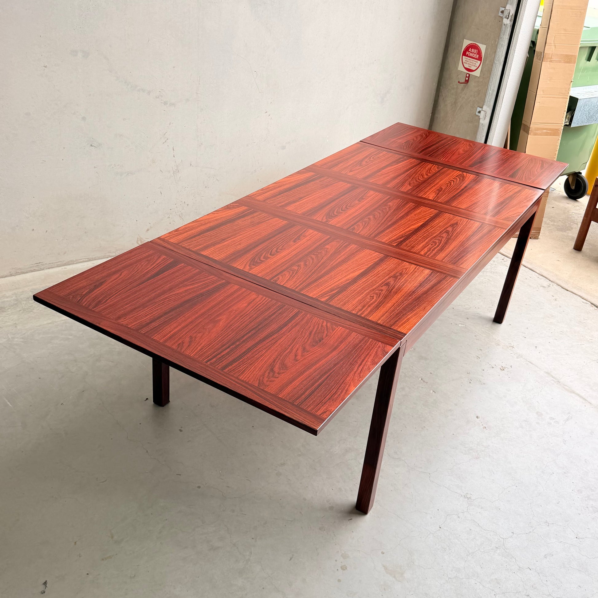 A 1970s Danish Modern Rosewood Dropleaf Dining Table (Model 166, 1975) by Vejle Stole og Mobelfabrik stands on four legs in a light-colored, empty room with concrete flooring.