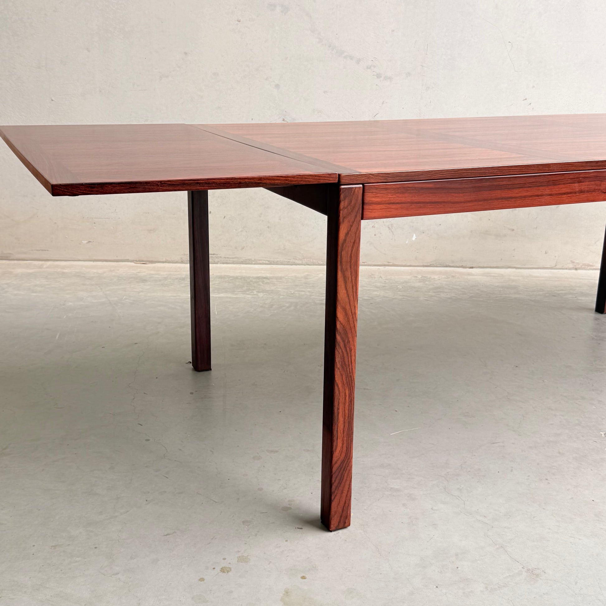 The 1970s Danish Modern Rosewood Dropleaf Dining Table by Vejle Stole og Mobelfabrik (Model 166, 1975) features clean lines and a rich wood grain finish, shown with one leaf extended against a light wall and concrete floor.