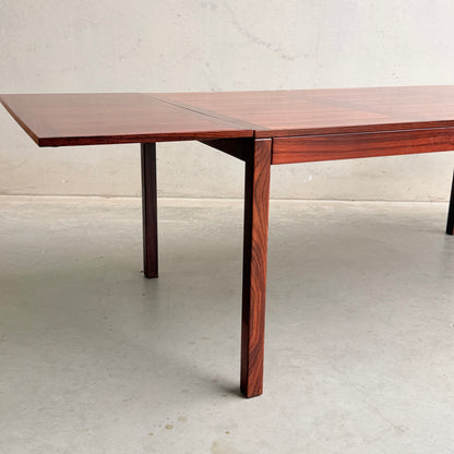 The 1970s Danish Modern Rosewood Dropleaf Dining Table by Vejle Stole og Mobelfabrik (Model 166, 1975) features clean lines and a rich wood grain finish, shown with one leaf extended against a light wall and concrete floor.
