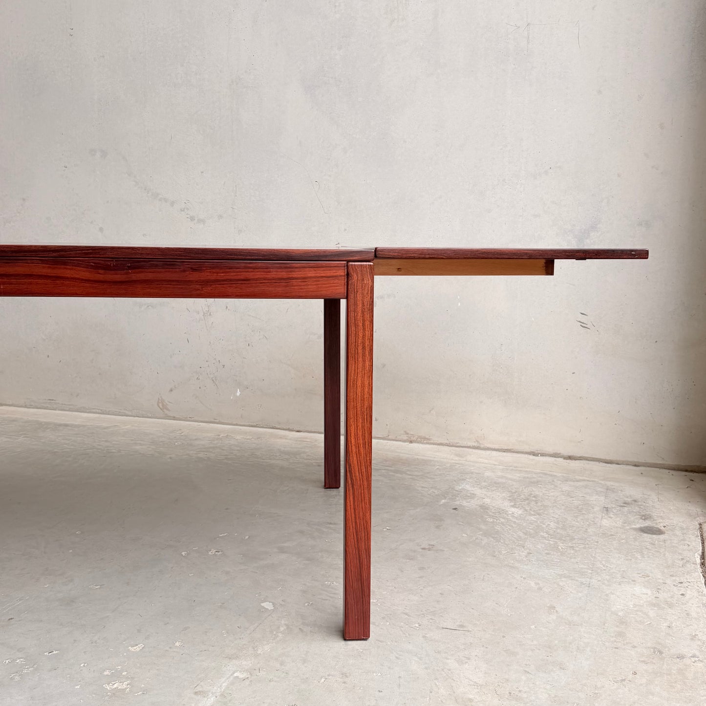 A 1970s Danish Modern Rosewood Dropleaf Dining Table (Model 166, 1975) by Vejle Stole og Mobelfabrik stands on a concrete floor against a light wall, with one extension leaf partially out and two legs visible.