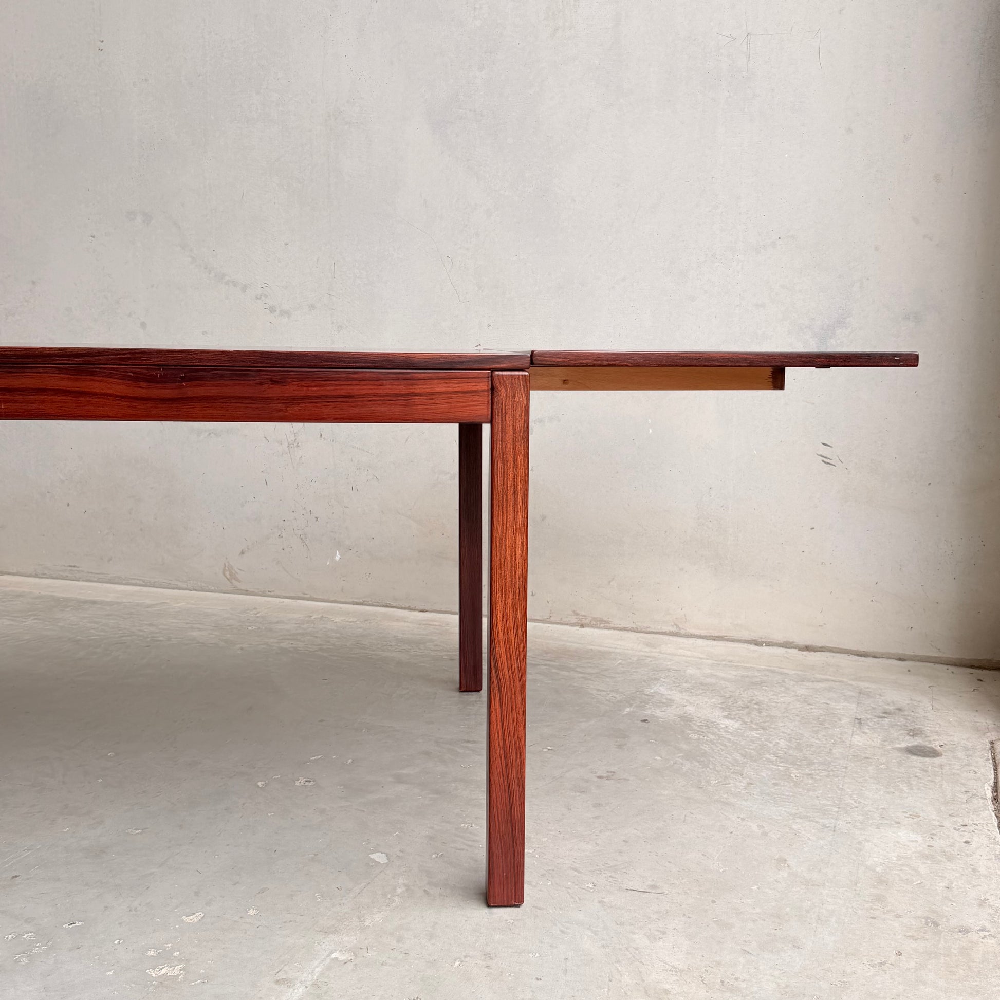 A 1970s Danish Modern Rosewood Dropleaf Dining Table (Model 166, 1975) by Vejle Stole og Mobelfabrik stands on a concrete floor against a light wall, with one extension leaf partially out and two legs visible.