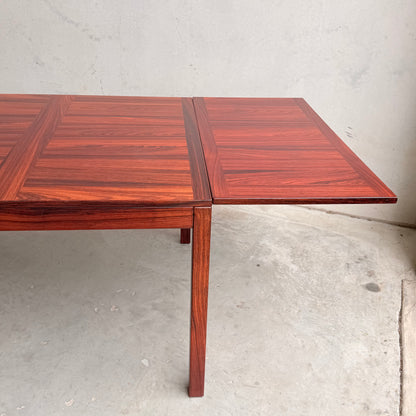 A close-up of the 1970s Danish Modern Rosewood Dropleaf Dining Table by Vejle Stole og Mobelfabrik (Model 166, 1975) with its rectangular extension leaf open, set on a light concrete floor against a plain, pale wall.