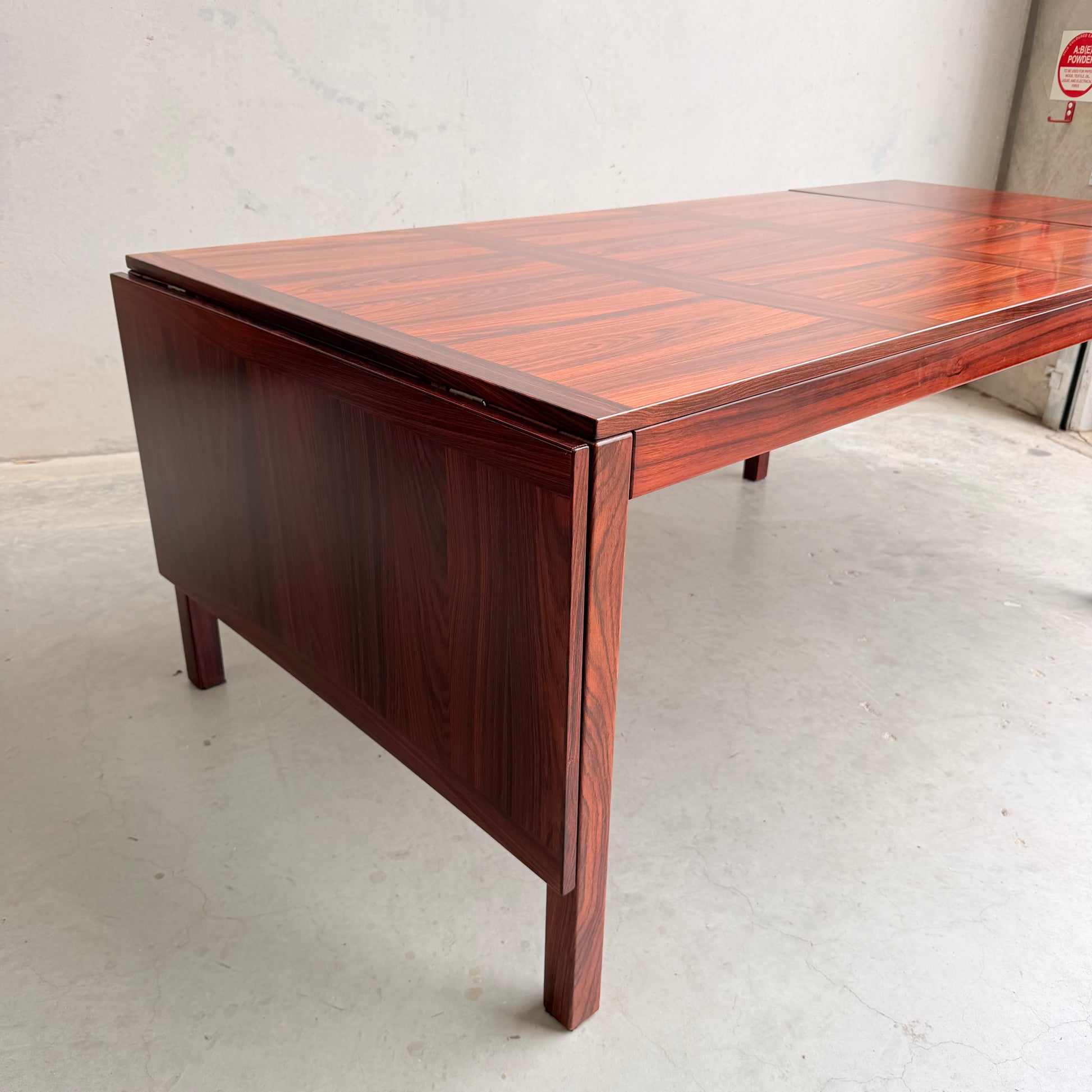 The 1970s Danish Modern Rosewood Dropleaf Dining Table by Vejle Stole og Mobelfabrik (Model 166, 1975) features a rich, reddish-brown finish and drop-leaf extension, perfectly capturing classic mid-century Danish design.