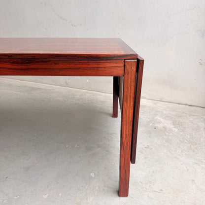 A close-up of the 1970s Danish Modern Rosewood Dropleaf Dining Table by Vejle Stole og Mobelfabrik (Model 166, 1975), featuring sleek straight legs and a polished finish, set against a light gray concrete floor and wall—timeless mid-century design.