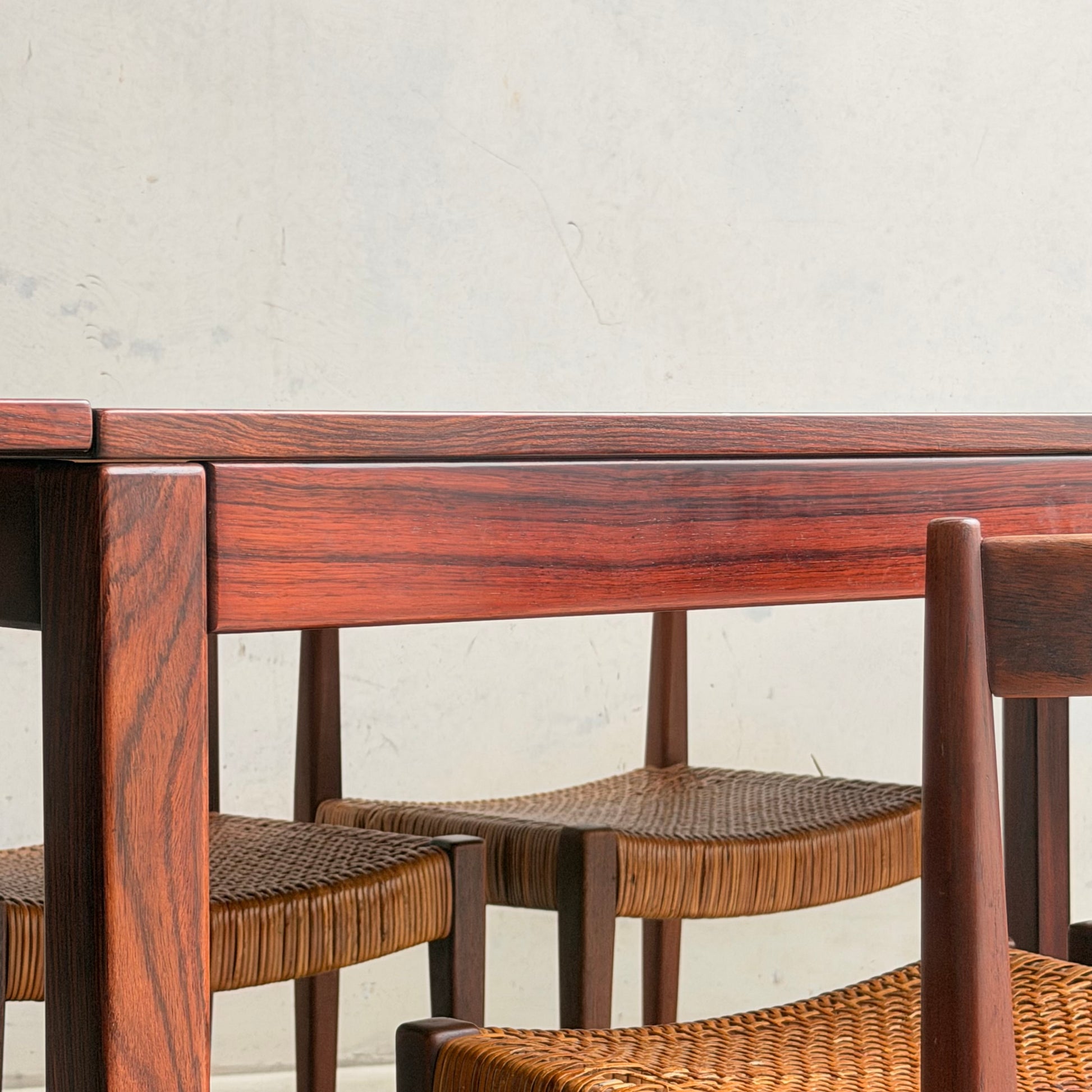 Close-up of a 1970s Danish Modern Rosewood Dropleaf Dining Table by Vejle Stole og Mobelfabrik (Model 166, 1975) with polished finish and chairs with woven seats, set against a light-colored textured wall.