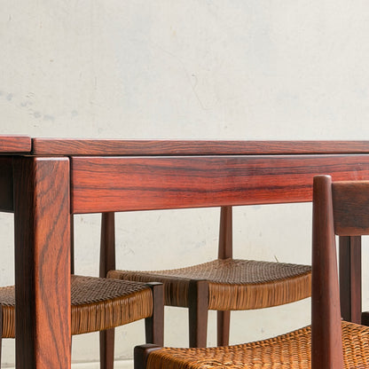 Close-up of a 1970s Danish Modern Rosewood Dropleaf Dining Table by Vejle Stole og Mobelfabrik (Model 166, 1975) with polished finish and chairs with woven seats, set against a light-colored textured wall.