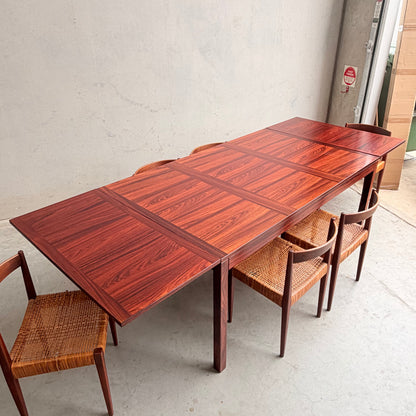A 1975 Danish Modern Rosewood Dropleaf Dining Table by Vejle Stole og Mobelfabrik (Model 166) is paired with six woven-seat chairs in a minimalist industrial space featuring concrete floors and walls.