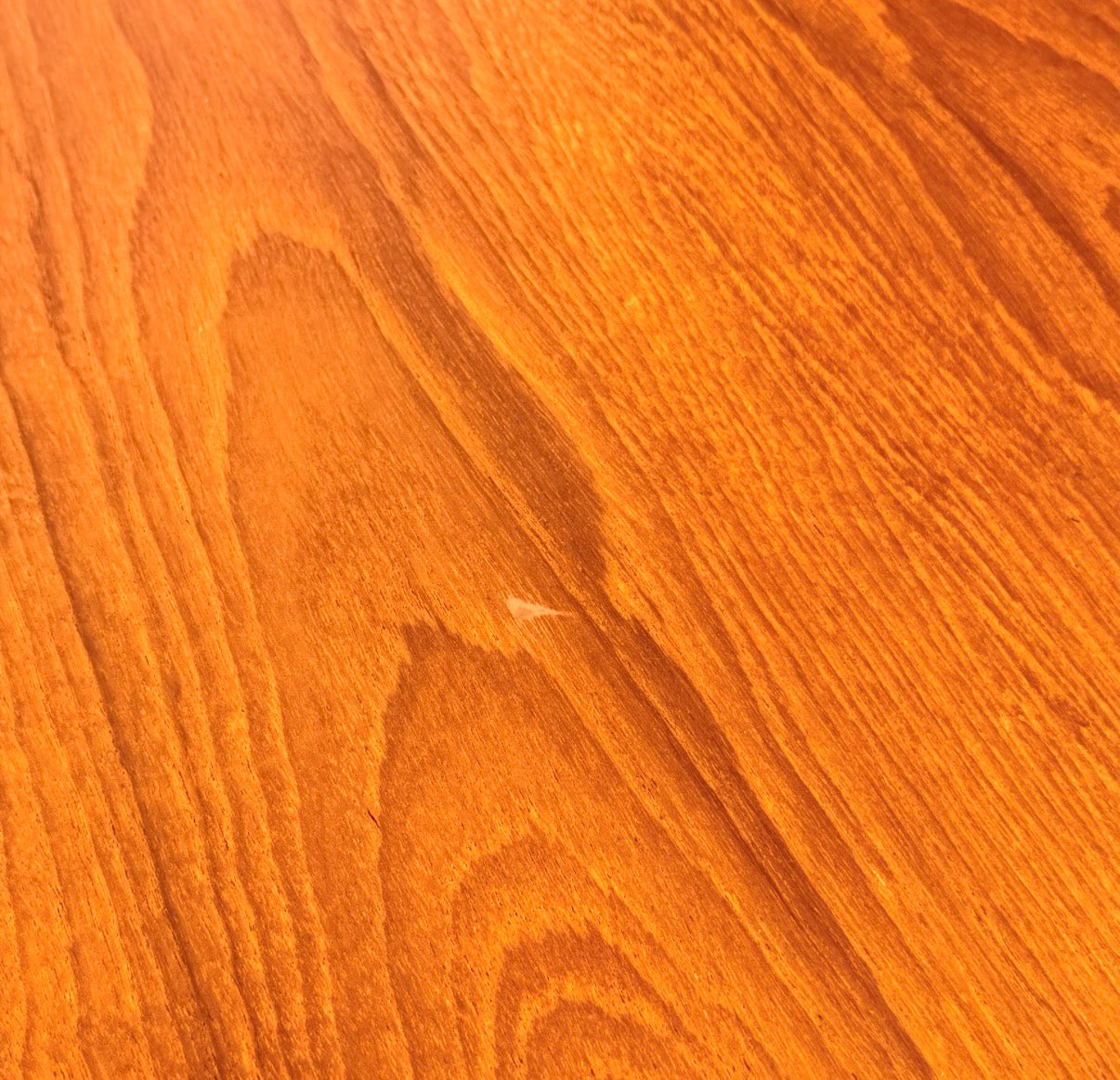 Close-up of a warm, orange-brown wooden surface with visible grain patterns—perfect for pairing with the Fully Restored Mid-Century Parker 91 Oval Teak Dining Suite and 6 Fler 64 Blackwood Chairs (Rediscover)—showing a small scratch near the center.