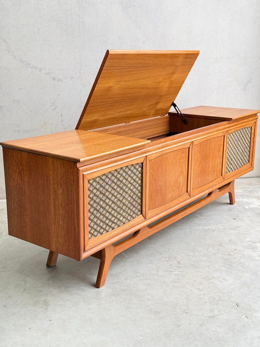 The General Electric Credenza - Spacemaker 250 is a fully converted teak TV and entertainment console with book-matched panels, angled legs, textured front design, and a hinged lid revealing storage—shown on a plain concrete floor.