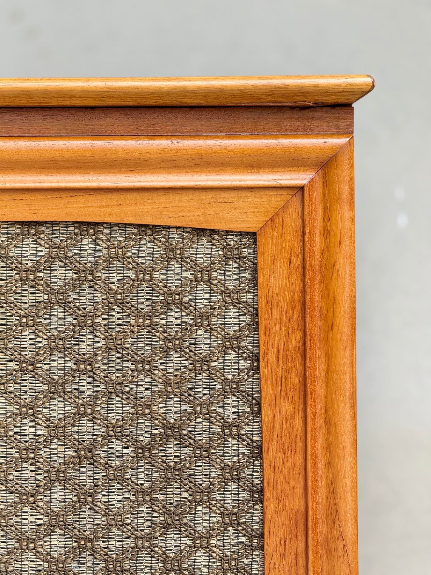 Close-up of the corner of a General Electric Credenza – Spacemaker 250, a fully converted teak TV/entertainment console, featuring a brown woven fabric panel against a plain, light background.