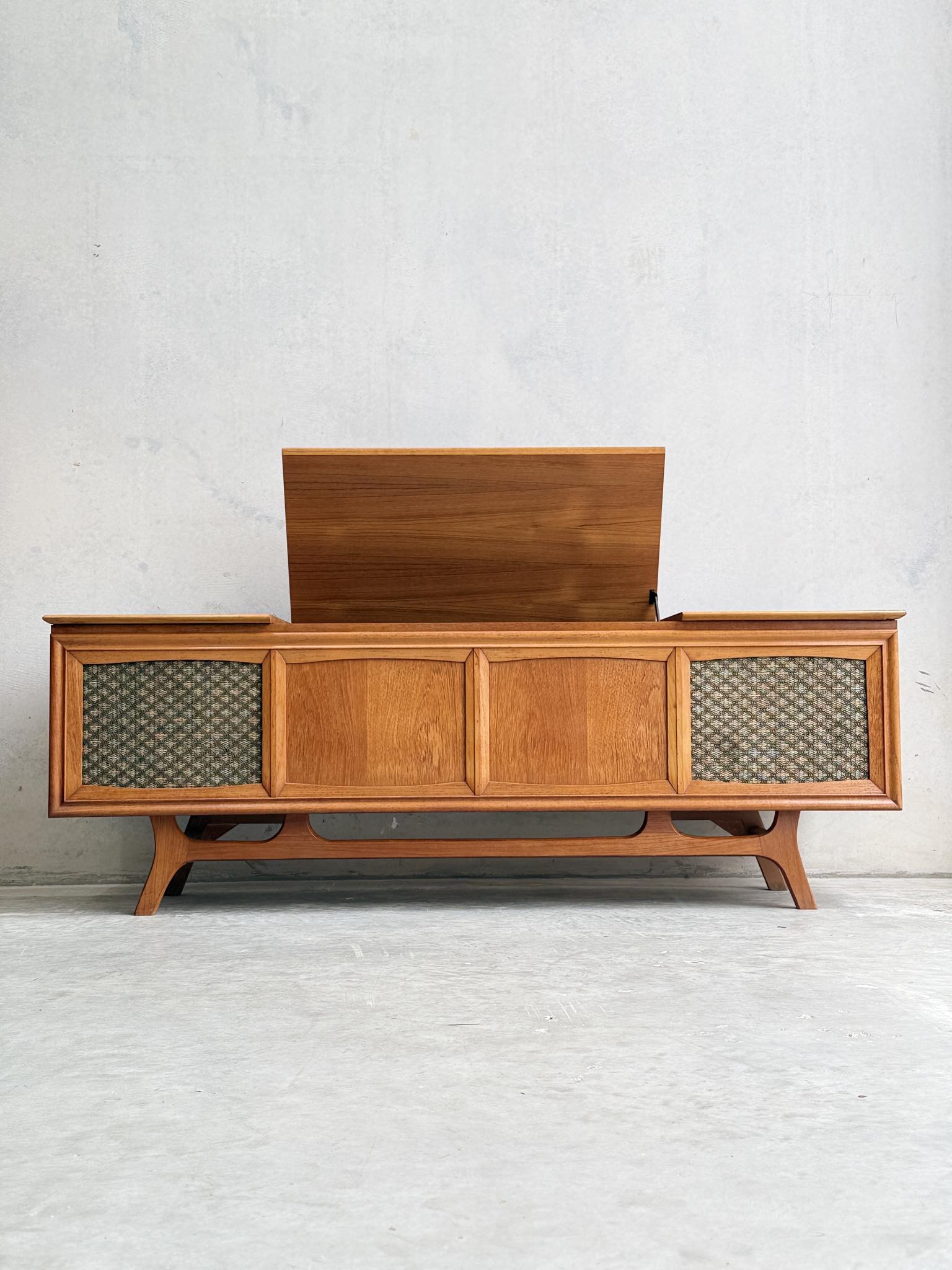 The General Electric Credenza - Spacemaker 250, a fully converted teak TV/entertainment console, features a lift-up lid and woven speaker grilles, and is set against a plain light gray wall.