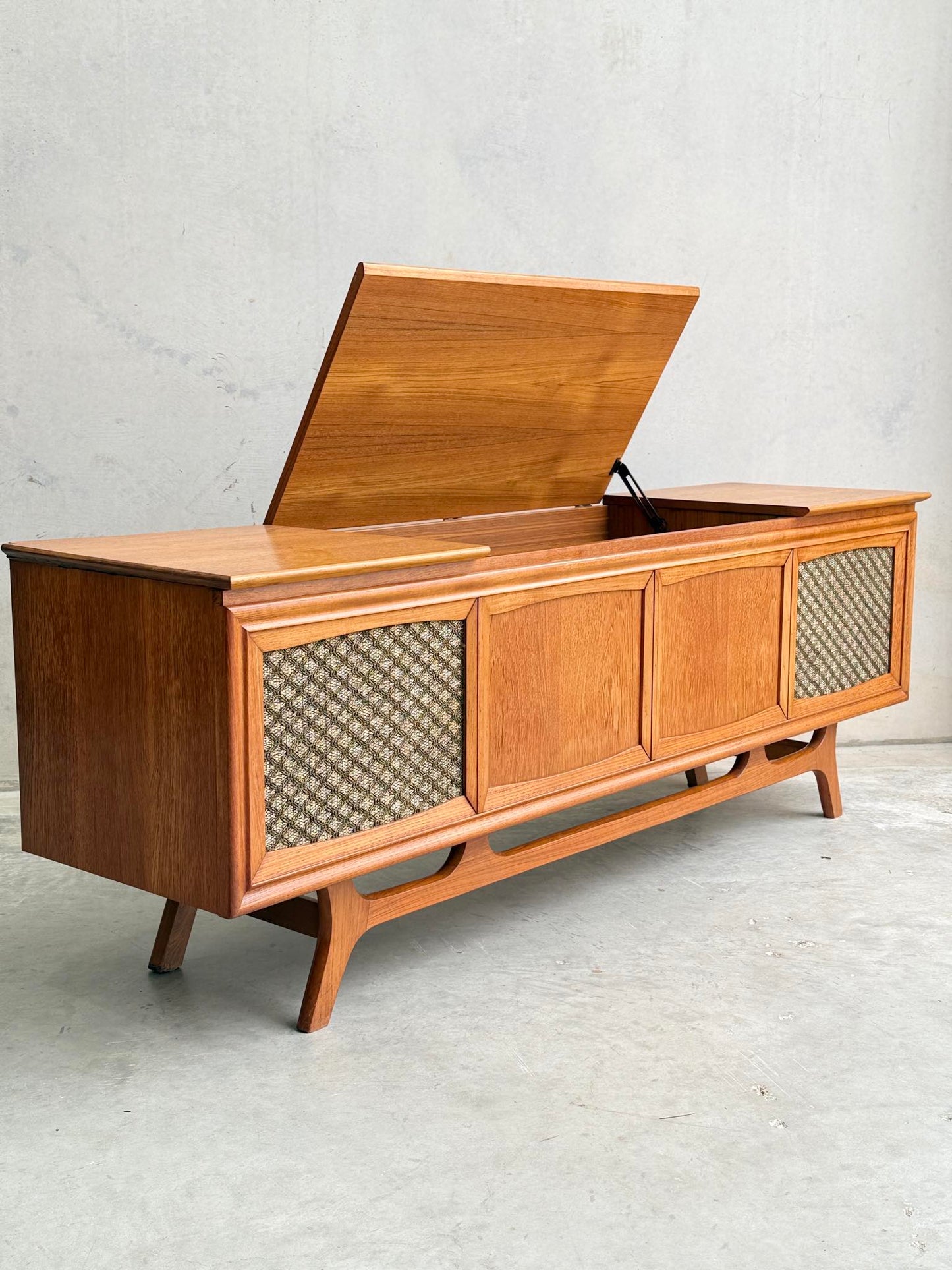 The General Electric Credenza - Spacemaker 250 is a fully converted teak TV/entertainment console featuring a hinged top lid for interior storage, patterned speaker fabric, solid wood doors, and short angled legs.