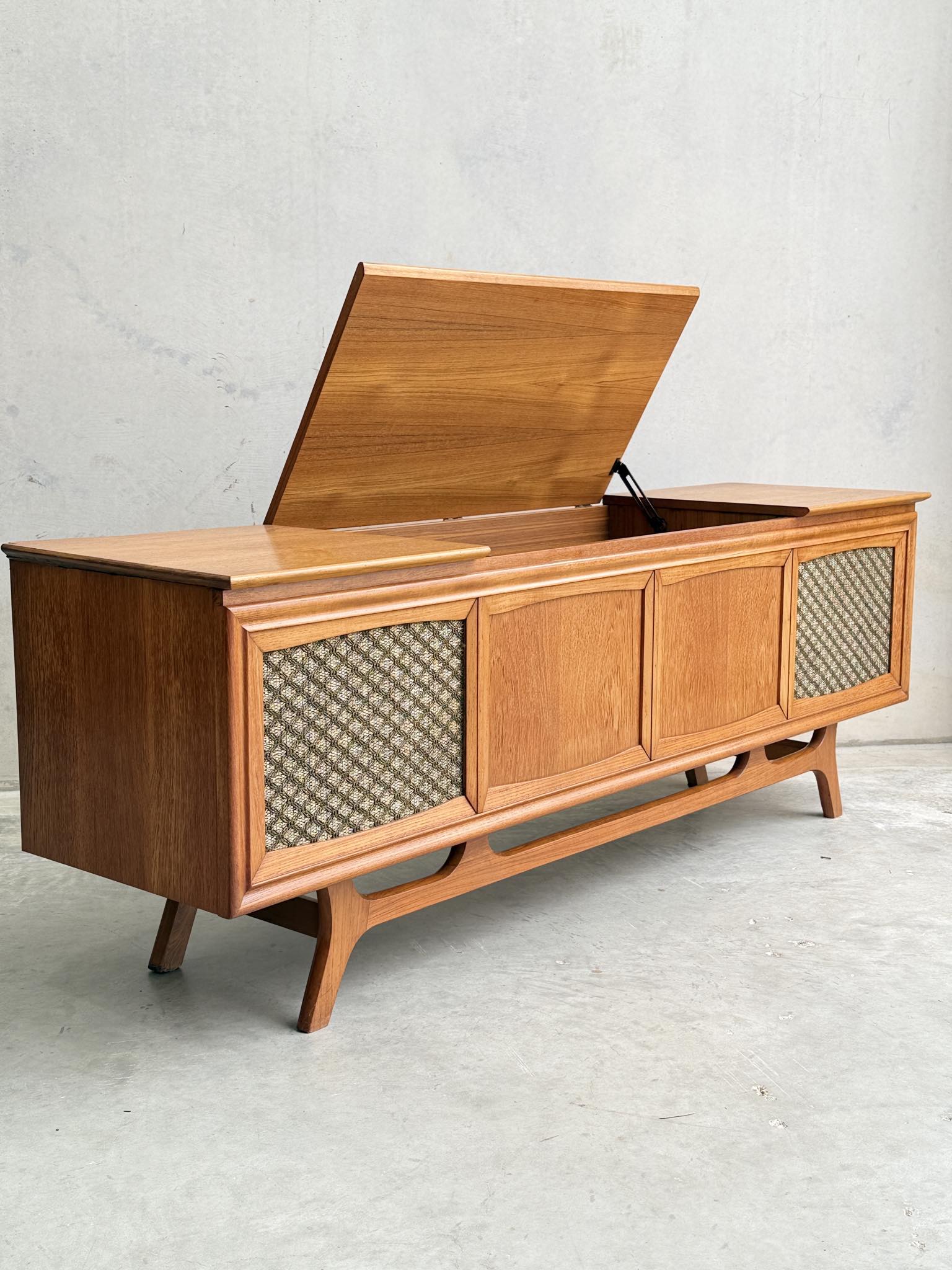 The General Electric Credenza - Spacemaker 250 is a fully converted teak TV/entertainment console featuring a hinged top lid for interior storage, patterned speaker fabric, solid wood doors, and short angled legs.