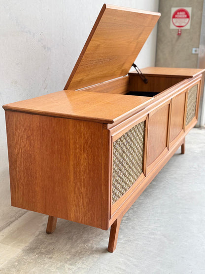 The General Electric Credenza - Spacemaker 250 is a fully converted teak TV and entertainment console with angled legs, a textured front panel, and a hinged top lid revealing interior storage, shown set against a concrete wall.