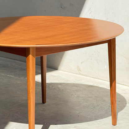 A Fully Restored Noblett Nordic Round MCM Table (Rediscover) stands on a smooth light gray floor against a pale wall, with sunlight casting strong shadows across the table and floor.