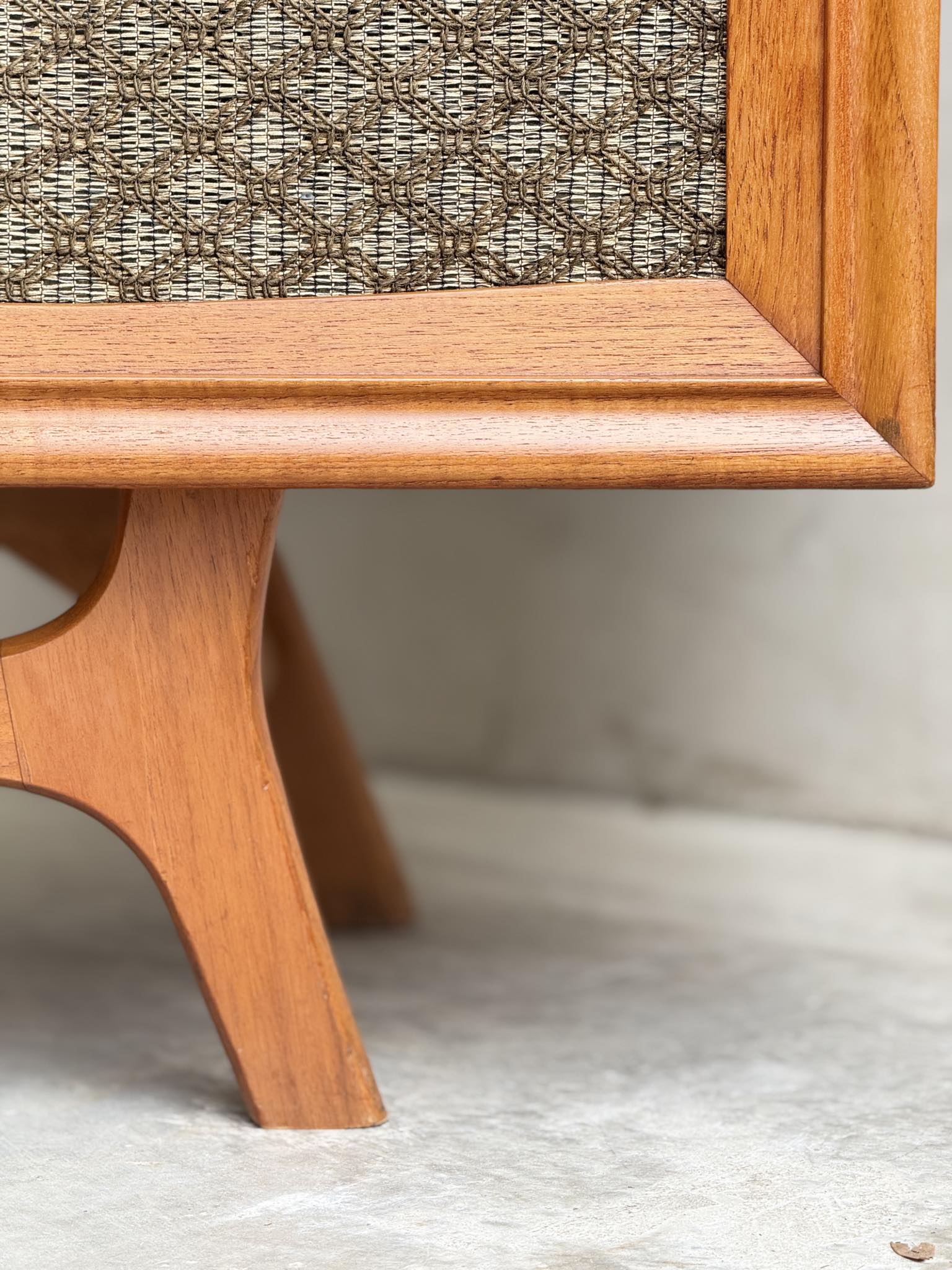 Close-up of the wooden leg and frame of the General Electric Credenza - Spacemaker 250, a fully converted teak TV/entertainment console, featuring textured fabric, light wood, and book-matched teak details on a neutral floor.
