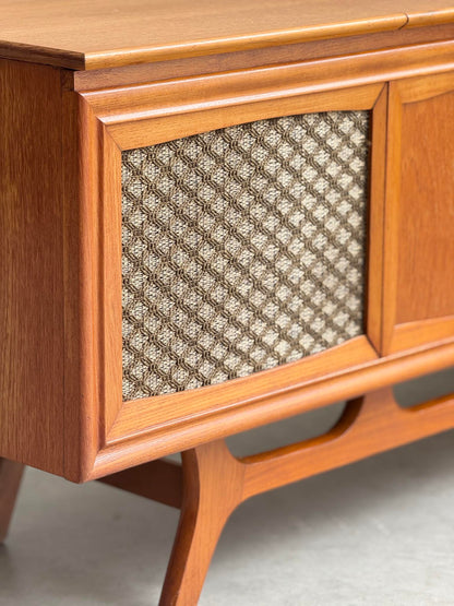 Close-up of a General Electric Credenza Spacemaker 250, a fully converted teak TV/entertainment console with mid-century modern design, featuring book-matched teak, angled legs, and a textured fabric panel on a light floor.