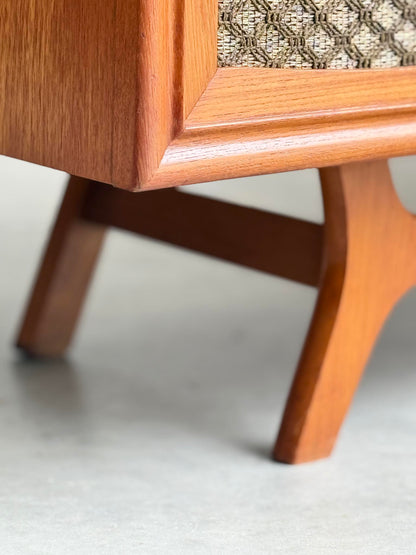 Close-up of the General Electric Credenza - Spacemaker 250’s book-matched teak leg, highlighting angled lines and a textured woven fabric panel above a smooth concrete floor.
