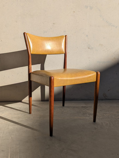 A set of six Parker Number 97 Dining Chairs in original mustard vinyl upholstery with dark wood legs and frame sits on a concrete floor against a plain, light-colored wall with visible shadows.