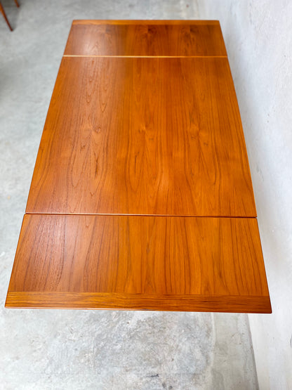 The Fully Restored Fler 64 Square Extension Table (Rediscover) features a warm wood finish and clean lines, showcased against a light gray concrete floor and a white wall.