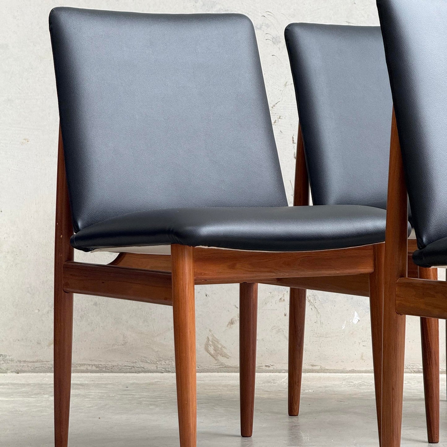 A set of four professionally restored Parker 118 Slab Back Chairs with black upholstered seats and wooden frames is displayed on a concrete floor against a light, textured wall. Pre-order available with a 25% non-refundable deposit.